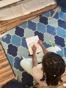 A child is writing on paper while sitting on the floor.