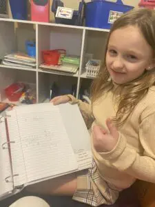 A girl holding up her hand in front of an open notebook.