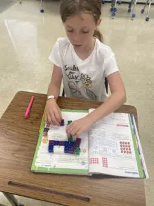 A girl sitting at a desk with a book and blocks.