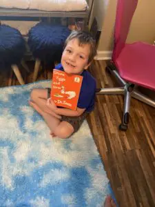A boy sitting on the floor holding a book.