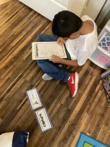 A boy is sitting on the floor and writing on a piece of paper.