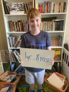 A boy holding a sign in front of a book shelf.