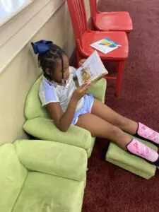 A young girl reading a book in a green chair.