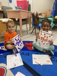 Two little girls sitting on the floor holding up numbers.