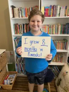 A boy holding a sign that says i grew 8 months in 8 weeks.