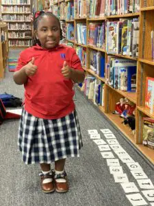A little girl in a red skirt standing in a library.